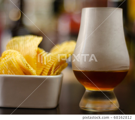 glass of whiskey with ice cubes and salty snacks 68162812