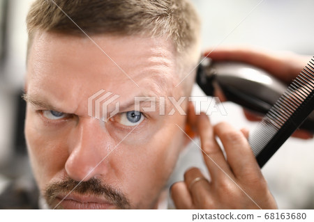 Man is being cut with clipper in hairdresser. 68163680