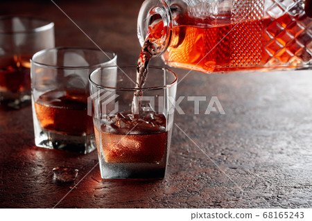 Pouring whiskey in glass with natural ice. 68165243