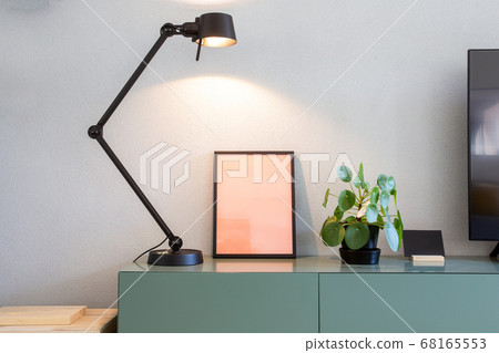 Stylish modern interior, empty picture frame with black lamp and green Chinese Money plant, retro pancake plant on green table scandinavian design Stylish modern interior, empty picture frame with black lamp and green Chinese Money plant, retro pancake plant on green table scandinavian design 68165553