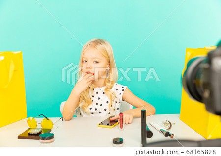 Happy girl sitting at the desk in the blue studio speaking in front of camera for vlog. Young beauty blogger recording video tutorial for Internet. 68165828