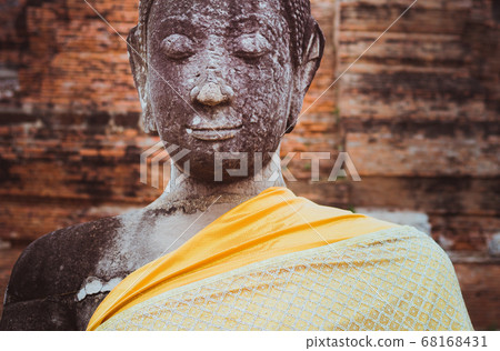 Buddha, a crumbling statue with the peaceful, meditative face and closed eyes, covered with orange cloth at Wat Mahathat in Ayutthaya. The art of Thailand. UNESCO World Heritage Site. 68168431