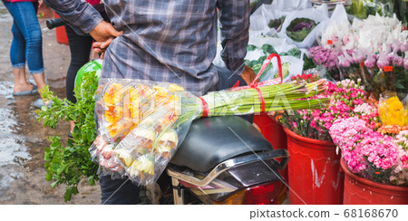 Ho Thi Ky Flower Market in Ho Chi Minh City (Saigon), Vietnam: a bouquet of flowers on a scooter seat behind a man waiting near buckets with flowers. An off-the-beaten-path travel attraction of Saigon 68168670