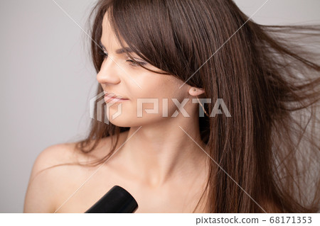 Beautiful smiling woman drying her long hair with dryer Beautiful smiling woman drying her long hair with dryer 68171353