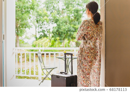 Tourist woman standing near window looking at beautiful garden view with her luggage in hotel bedroom. Tourist woman standing near window looking at beautiful garden view with her luggage in hotel bedroom. 68178113
