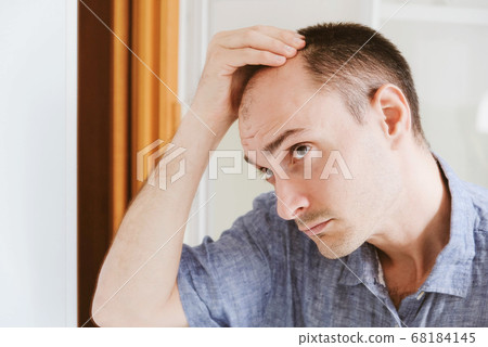 Young man looking at mirror worry about balding. Young man looking at mirror worry about balding. 68184145