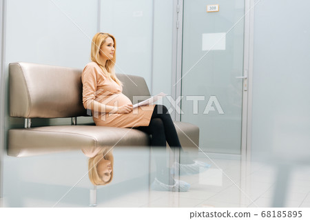 Serious young pregnant woman is sitting in hallway of hospital waiting to see gynecologist. Serious young pregnant woman is sitting in hallway of hospital waiting to see gynecologist. 68185895