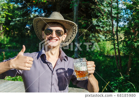 young man in a hat and sunglasses with a mug of young man in a hat and sunglasses with a mug of 68185980