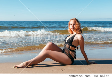 young blonde girl in a black swimsuit sits on the sand of the sea shore young blonde girl in a black swimsuit sits on the sand of the sea shore 68186146