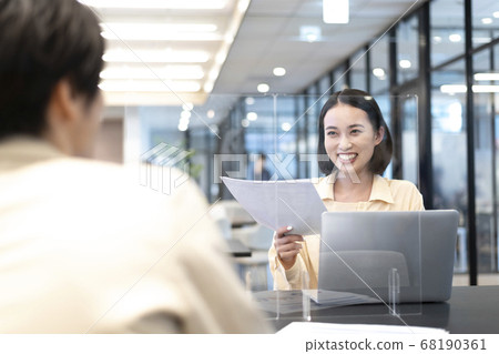 A female employee who is trying to get a colleague to see the material through an acrylic plate while laughing a little at the face-to-face work after a long absence A female employee who is trying to get a colleague to see the material through an acrylic plate while laughing a little at the face-to-face work after a long absence 68190361
