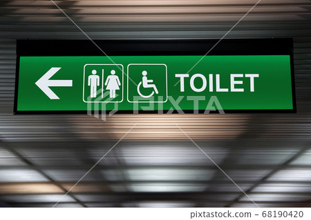 green restroom or toilet sign with arrow hang from ceiling at public area 68190420