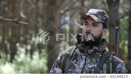 Portrait of handsome young man hunter or tourist. Man in camouflage clothes hunts outdoor in forest hunting alone. Close up of man hiker standing in forest. Hunter hunts down prey. 68190623