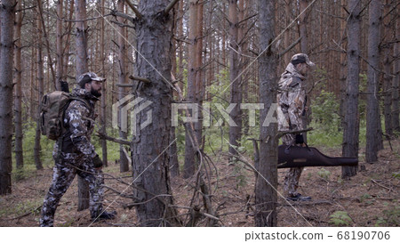Two hunter men in camouflage clothes with guns walking through forest during hunting season. Man hunter outdoor in forest hunting. Hunters hunt down prey and follow trail of animals Two hunter men in camouflage clothes with guns walking through forest during hunting season. Man hunter outdoor in forest hunting. Hunters hunt down prey and follow trail of animals 68190706