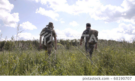 Fishermen go fishing. Relaxed men spending leisure together and going for fishing on river. View from back of walking men in camouflage with fishing rods. Fishermen go fishing. Relaxed men spending leisure together and going for fishing on river. View from back of walking men in camouflage with fishing rods. 68190707