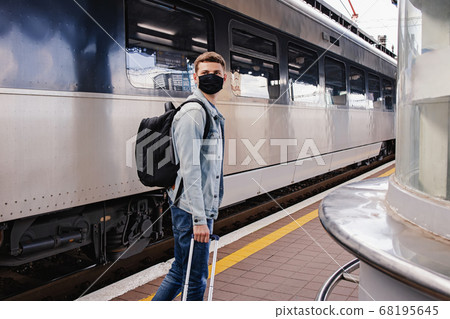 Young man wearing protective face mask standing on the railway station near the train. 68195645
