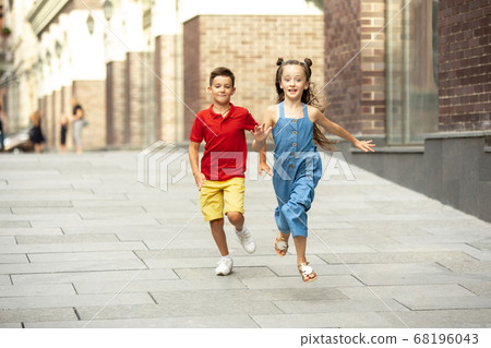 Two smiling kids, boy and girl running together in town, city in summer day Two smiling kids, boy and girl running together in town, city in summer day 68196043