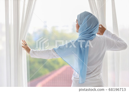 asian muslim woman wearing white sleepwear, stretching her arms after getting up in the morning 68196713