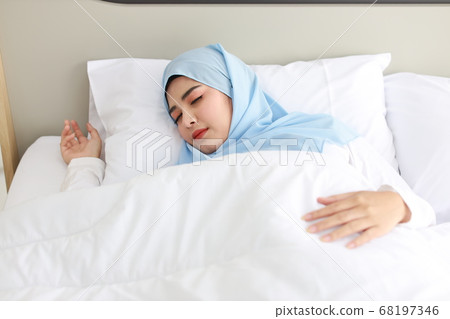 Oversleeping asian muslim woman wearing white sleepwear lying on bed with happiness. Oversleeping asian muslim woman wearing white sleepwear lying on bed with happiness. 68197346