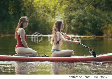 Two women sailing on the inflatable boat on river and using a paddle Two women sailing on the inflatable boat on river and using a paddle 68198872