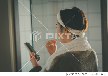 A woman brushing teeth while looking at a smartphone A woman brushing teeth while looking at a smartphone 68201372