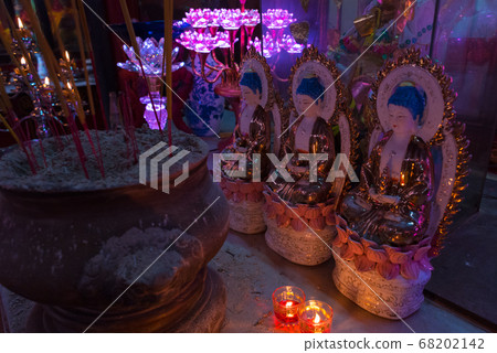 Obscure temple interior with incense sticks, candles, statues lit with purple lamp light in Tam Son Pagoda, Cho Lon (Saigon's Chinatown). Obscure temple interior with incense sticks, candles, statues lit with purple lamp light in Tam Son Pagoda, Cho Lon (Saigon's Chinatown). 68202142
