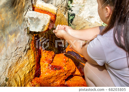 Young woman taps the water from spring of mineral water, ferruginous water with a high mineral content Young woman taps the water from spring of mineral water, ferruginous water with a high mineral content 68203805
