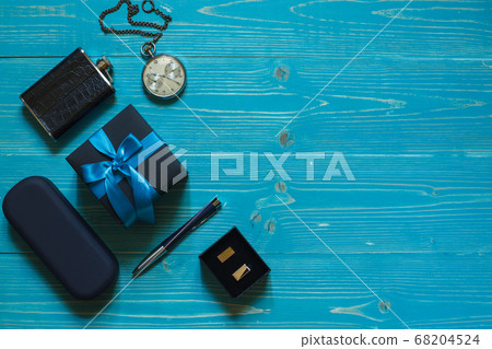 A gift with a blue ribbon, a pocket watch on a chain, cufflinks and a case with glasses on a blue background A gift with a blue ribbon, a pocket watch on a chain, cufflinks and a case with glasses on a blue background 68204524