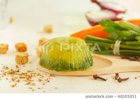 A portion of frozen green broth close-up, cooking ingredients in the background 68205051