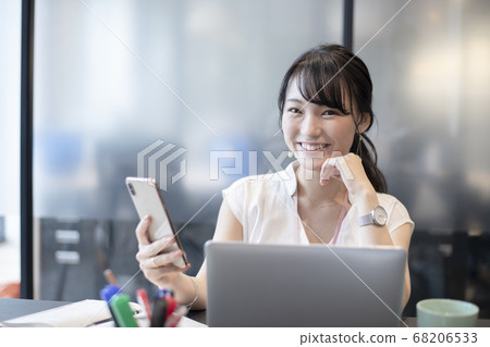 A woman who enjoys operating a smartphone in the office A woman who enjoys operating a smartphone in the office 68206533