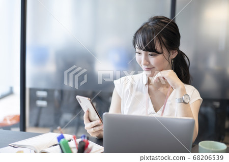 A woman who enjoys operating a smartphone in the office A woman who enjoys operating a smartphone in the office 68206539