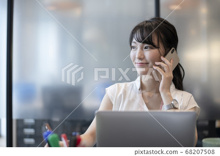 一個女人打電話給在個人電腦前的智能手機 68207508