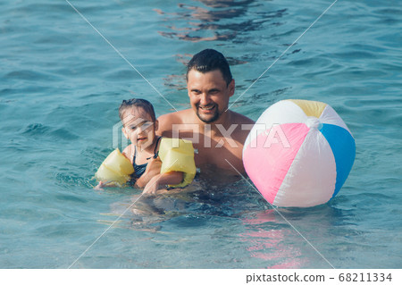A young father and daughter swim in the sea. swimming training. ball game A young father and daughter swim in the sea. swimming training. ball game 68211334