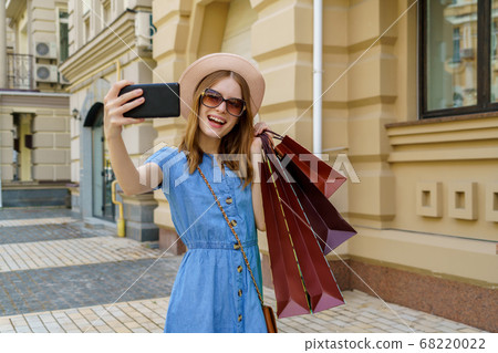 Young Woman with shopping bags making selfie walking in a city at summer day Young Woman with shopping bags making selfie walking in a city at summer day 68220022