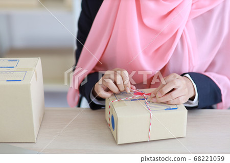 Active smiling asian muslim woman in blue suit sitting and working with online package box delivery 68221059