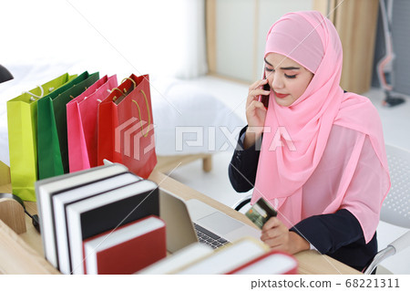 asian muslim woman sitting and holding credit card using mobile phone for payment online purchasing asian muslim woman sitting and holding credit card using mobile phone for payment online purchasing 68221311