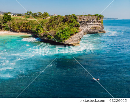 Surfing waves in blue ocean and cliff at background. Aerial view of tropical island with waves Surfing waves in blue ocean and cliff at background. Aerial view of tropical island with waves 68226025