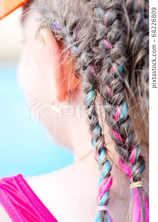 A lot of braided colored plaits on a girl's head. 68226809