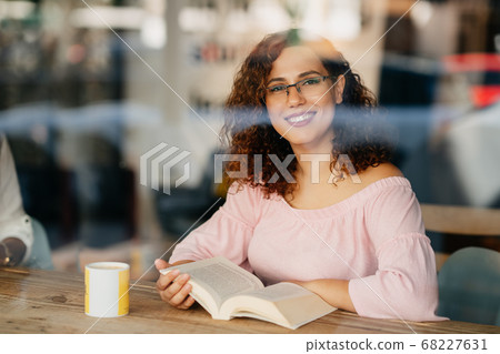 Young woman with eyeglasses reading book in cafe Young woman with eyeglasses reading book in cafe 68227631