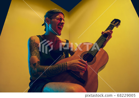 Young caucasian musician inspired performing on yellow background in neon light Young caucasian musician inspired performing on yellow background in neon light 68229005