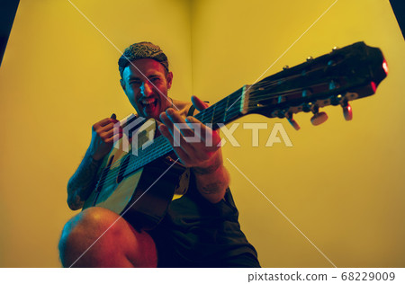 Young caucasian musician inspired performing on yellow background in neon light Young caucasian musician inspired performing on yellow background in neon light 68229009