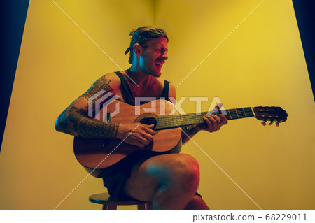Young caucasian musician inspired performing on yellow background in neon light Young caucasian musician inspired performing on yellow background in neon light 68229011