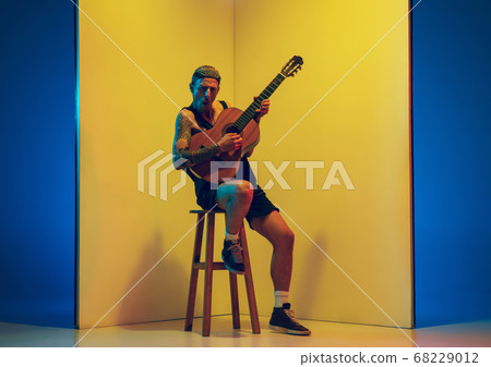 Young caucasian musician inspired performing on yellow background in neon light Young caucasian musician inspired performing on yellow background in neon light 68229012