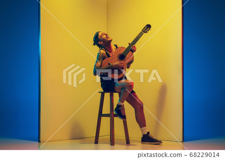 Young caucasian musician inspired performing on yellow background in neon light 68229014