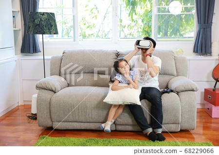 Happy Asian family father and daughter play virtual reality goggles on the sofa in the living room Happy Asian family father and daughter play virtual reality goggles on the sofa in the living room 68229066