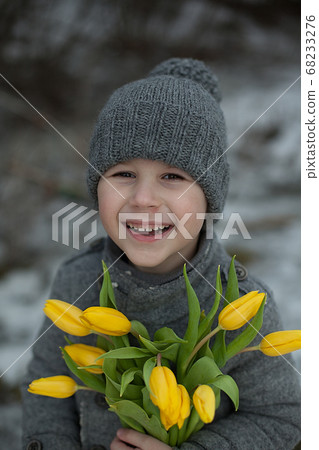 A handsome boy in a gray coat congratulates on the holiday with large bouquets of yellow tulips. March 8, Mother's Day, Women's Day, Gift, surprise, emotions. A handsome boy in a gray coat congratulates on the holiday with large bouquets of yellow tulips. March 8, Mother's Day, Women's Day, Gift, surprise, emotions. 68233276