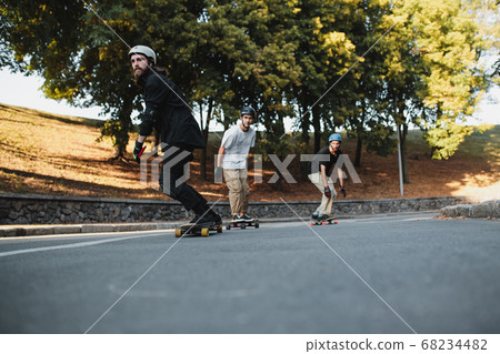 Three charismatic guys ride longboards. Bottom view. Three charismatic guys ride longboards. Bottom view. 68234482