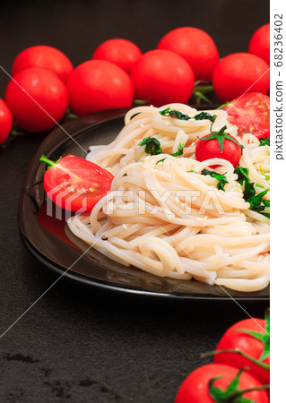 spaghetti with spinach, tomatoes, sesame seeds on a black table on a black plate. close up, copy space spaghetti with spinach, tomatoes, sesame seeds on a black table on a black plate. close up, copy space 68236402
