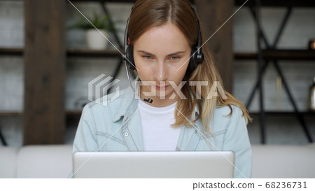 Young woman with a headset working online on computer while sitting at home. Concept of studying or working from home online Young woman with a headset working online on computer while sitting at home. Concept of studying or working from home online 68236731
