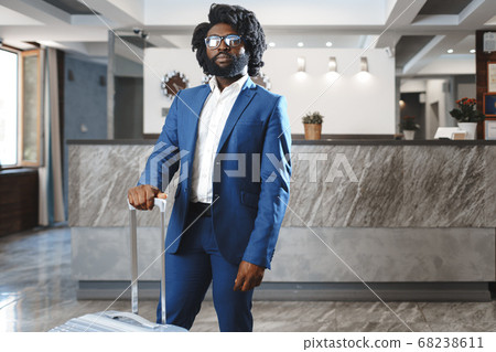 Black businessman with packed luggage standing in hotel lobby 68238611