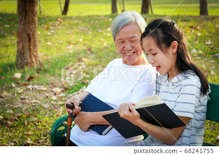 Happy asian granddaughter reading a book and senior grandmother together at summer park,loving child girl holding book sitting on bench having fun reading interesting book and telling story to elderly Happy asian granddaughter reading a book and senior grandmother together at summer park,loving child girl holding book sitting on bench having fun reading interesting book and telling story to elderly 68241755
